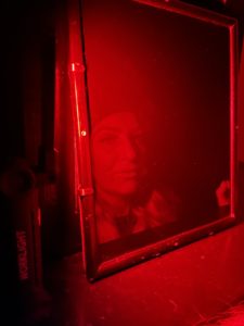 Illuminated In Red, Night Supervisor Kate casts her gaze into a mirror waiting for the unknown to happen.