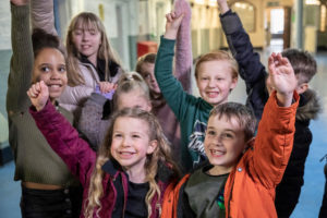 A group of children smiling with their hands up