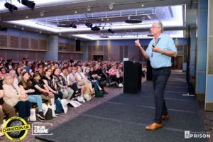 Speaker talking to an audience in a hall during CrimeCon 2023
