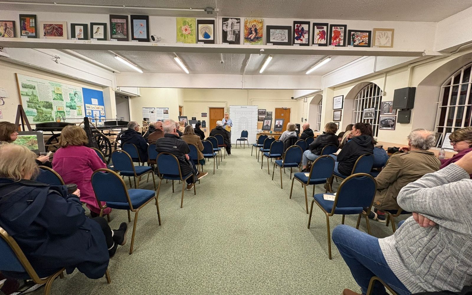 A room with a small audience facing the front with a presenter delivering the event
