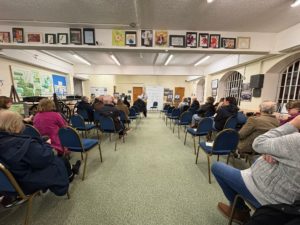 A room with a small audience facing the front with a presenter delivering the event