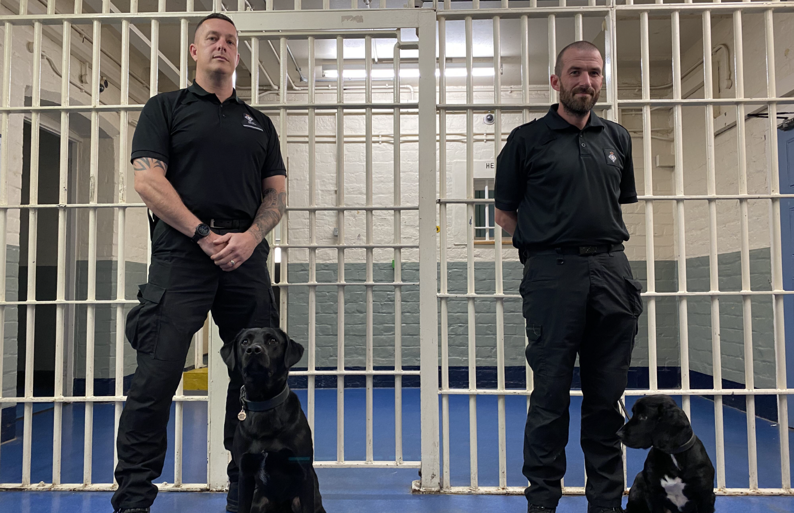 Two male handlers and their work dogs pictured on prison landings