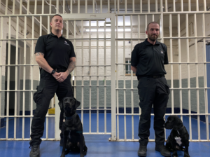 Two male handlers and their work dogs pictured on prison landings